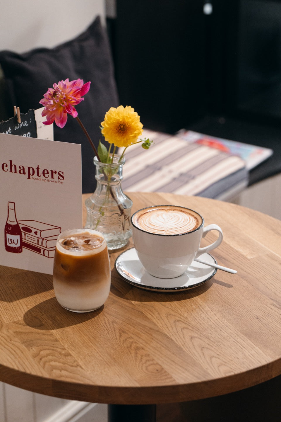 A flat white and an iced latte on a table at Chapters, with the menu card and flowers